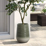 A green-leaved tree nestled in a ribbed ceramic planter with a drainage hole stands on a tiled patio near a sliding glass door, seamlessly enhancing both indoor and outdoor environments, with stylish outdoor furniture in the background.