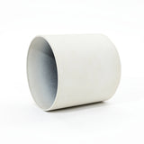 A contemporary, durable white ceramic planter lies on its side against a plain background, showcasing its sleek cylindrical design.