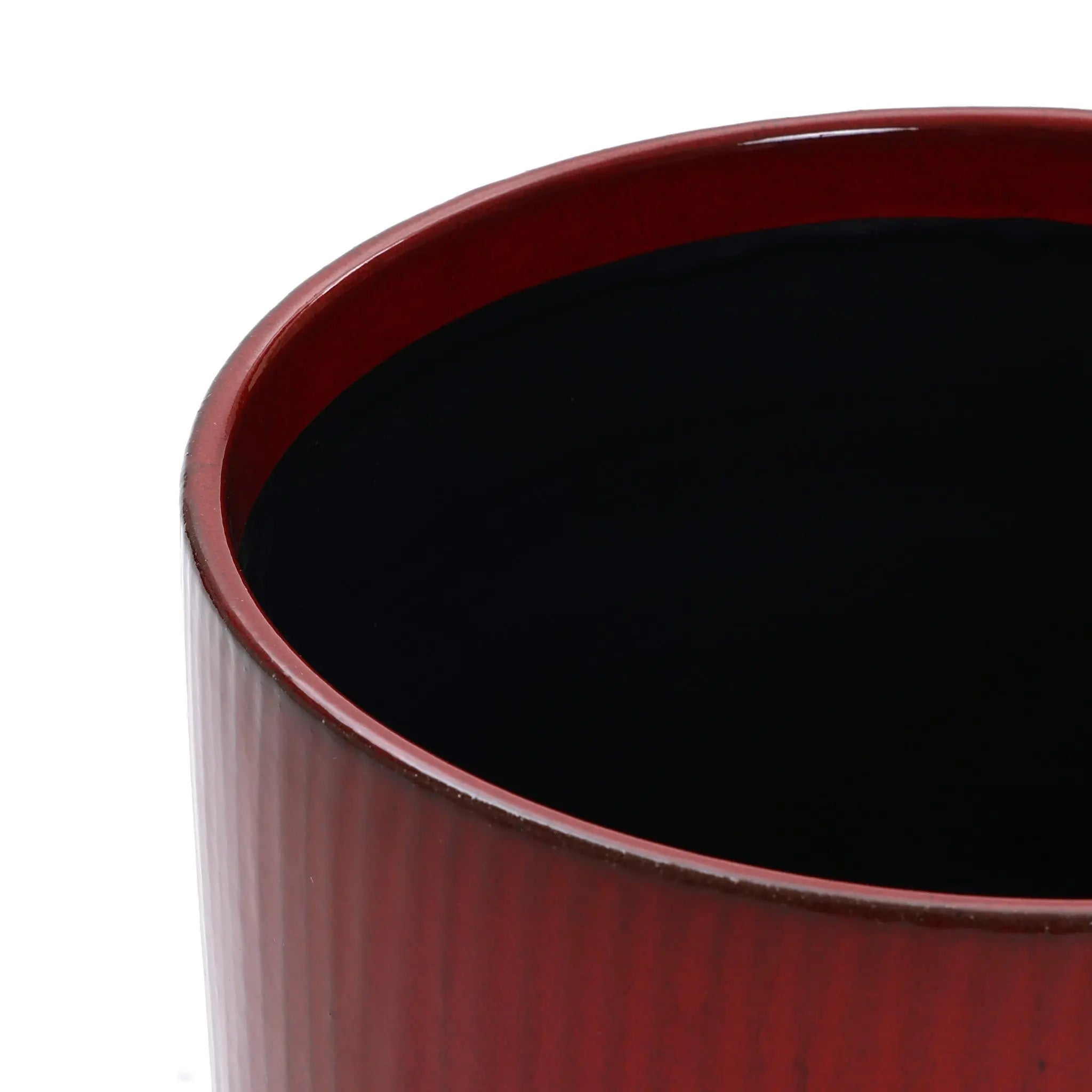 A close-up of the LuxenHome Burgundy red glazed ceramic planter showcases its glossy exterior with a textured vertical stripe design. The interior is a smooth, dark black that contrasts with the slightly rounded rim, creating a striking look for this 10.83 high round planter.
