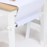 The LuxenHome Children Play Table with Bookcase and 2 Chairs Set includes a white arts and crafts table with a wooden top and a roll of white paper mounted underneath, unrolling onto the surface for crafting or drawing.