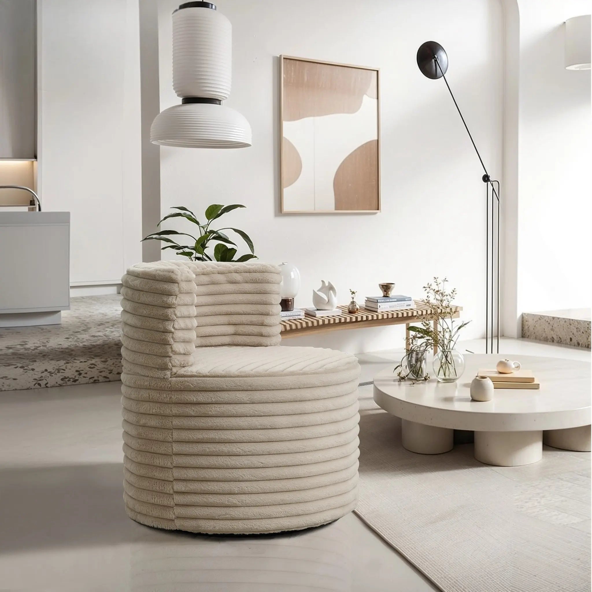 A modern living room showcases a LuxenHome Brie camel swivel barrel accent chair, a round coffee table with decor, and a minimalist floor lamp. A potted plant adds greenery while abstract art adorns the wall. Soft, neutral tones create an inviting atmosphere.