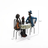 Two metal figures, capturing romantic moments, sit at a small round table draped in a floral-patterned cloth, adorned with a vase of red flowers. This modern brown resin couple decoration measures 9.4 tall, 9.4 wide, and 5.2 deep—a perfect wedding gift.