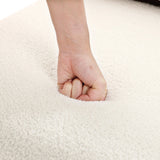A close-up shows a hand pressing into the plush, white surface of the LuxenHome Lorenzo boucle upholstered wood frame armless accent chair, creating an indentation. The high-density foam offers cushiony comfort and softness with mid-century allure.