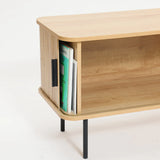 This wooden cabinet, featuring open shelving and a side section for books, stands elegantly on black metal legs. With its design reminiscent of an oak TV stand, it offers ample space to accommodate a 65-inch TV while maintaining a stylish appearance.