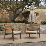 Two FSC-certified wooden chairs with cushions grace the patio, featuring a stylish rope back design. They sit on a rug near an umbrella, surrounded by lush potted plants, with a stone wall and tree in the background.