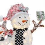A smiling snowman wearing a red Santa hat and a black-and-white checkered scarf holds a green gift box covered in snow—perfect as an outdoor Christmas decor snowman decoration.