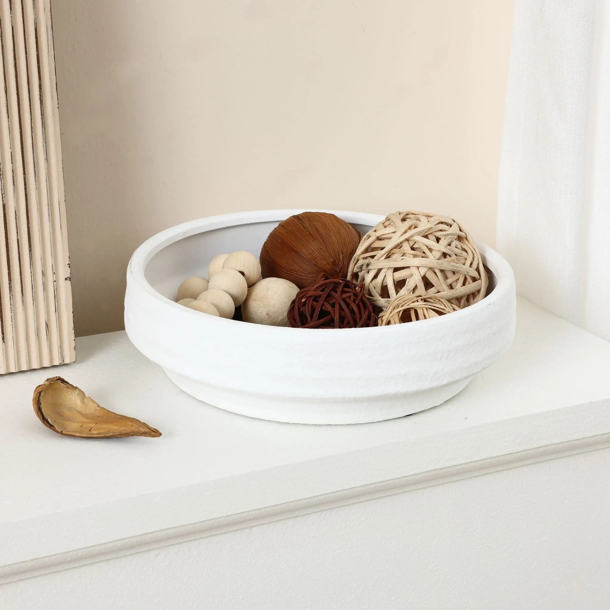 A white decorative bowl features various textured balls with a small dried leaf beside it, echoing the elegance of a round bowl vase in its simplicity.