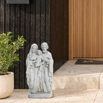 A Holy Family statue crafted from marble-like polyresin stands on a stone step beside a potted plant against a wooden wall, adding a touch of religious decor to the serene setting.