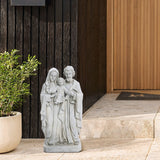 A Holy Family statue crafted from marble-like polyresin stands on a stone step beside a potted plant against a wooden wall, adding a touch of religious decor to the serene setting.