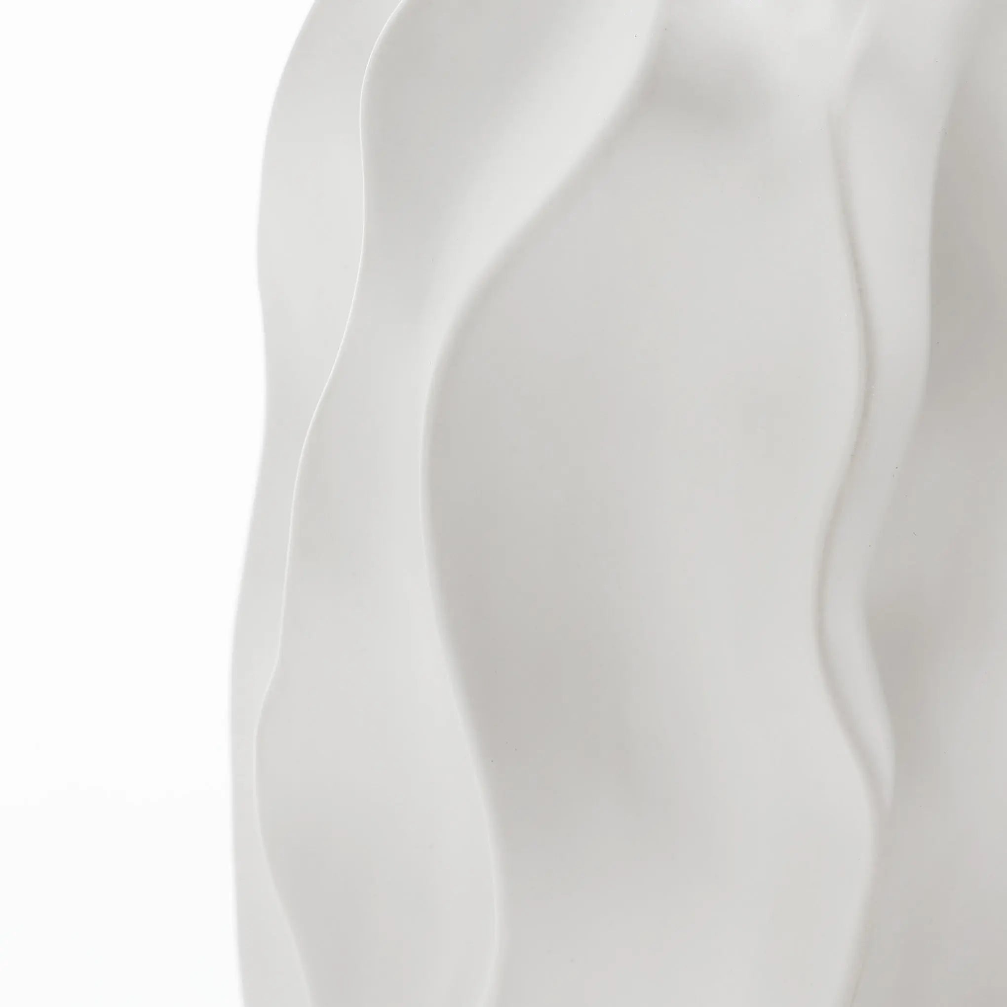 Close-up of a white, wavy-textured surface, resembling abstract flowing shapes or smooth fabric folds, echoing the elegant design of a ceramic vase.