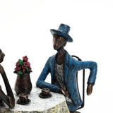 Sculpted figures capturing romantic moments sit at a table with coffee cups and a vase of flowers. One figure wears a blue coat and hat, embodying modern brown resin couple decoration perfect for a wedding gift.