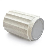 A cylindrical, light gray cement object with vertical grooves lies on its side against a white background—perfect as modern side table or outdoor decor.