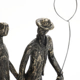 A textured sculpture of two figures, crafted from modern resin, features one holding a balloon. The figures appear to be wearing hats and walking together, making it a charming home decoration.