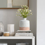 A vase with small white flowers graces a stack of books on the shelf. Nearby, a stoneware vase and a two-tone ceramic vase add texture and charm to the display.