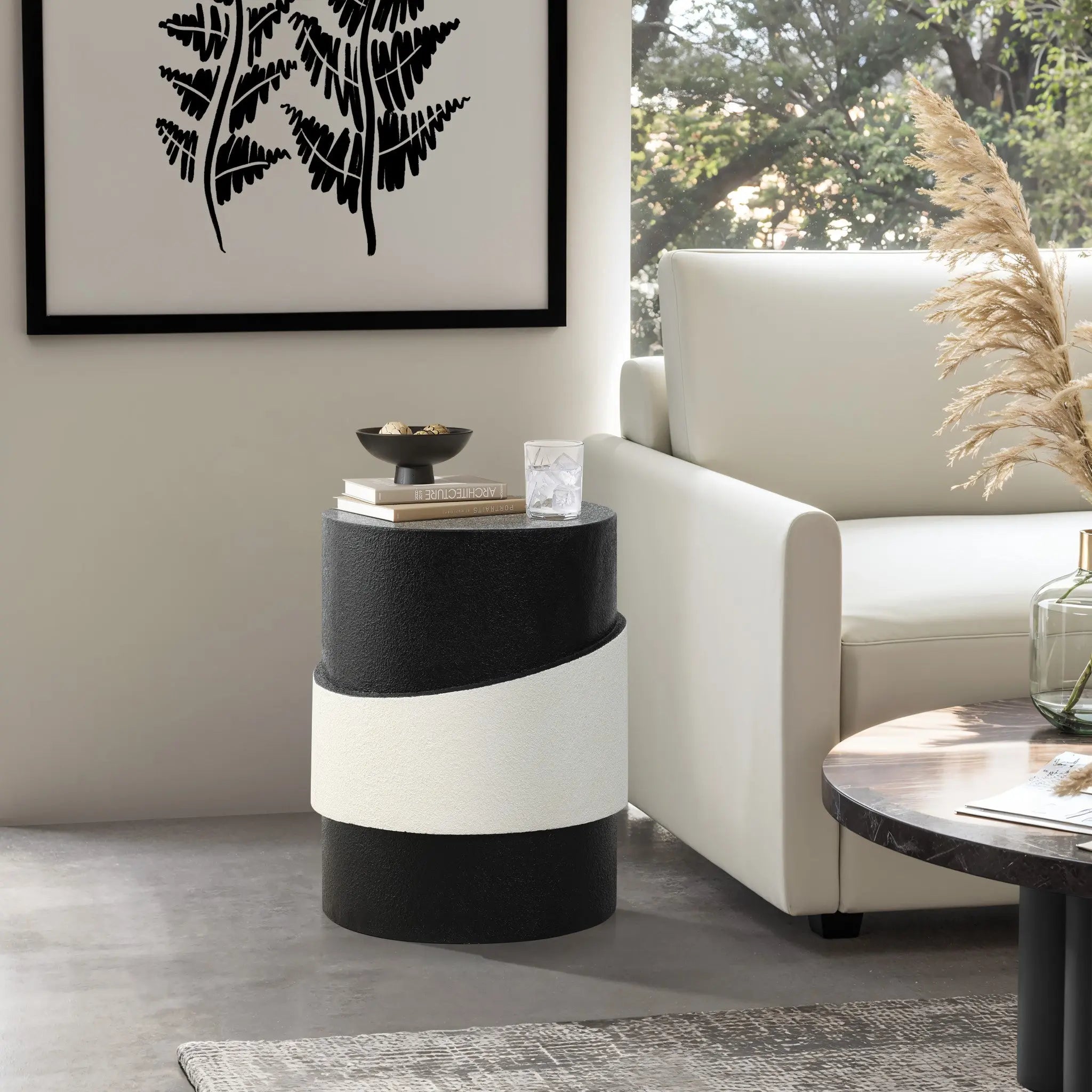 A modern living room features a black and white cylindrical side table with a unique white irregular pattern, a white sofa, wall art, and a round coffee table.