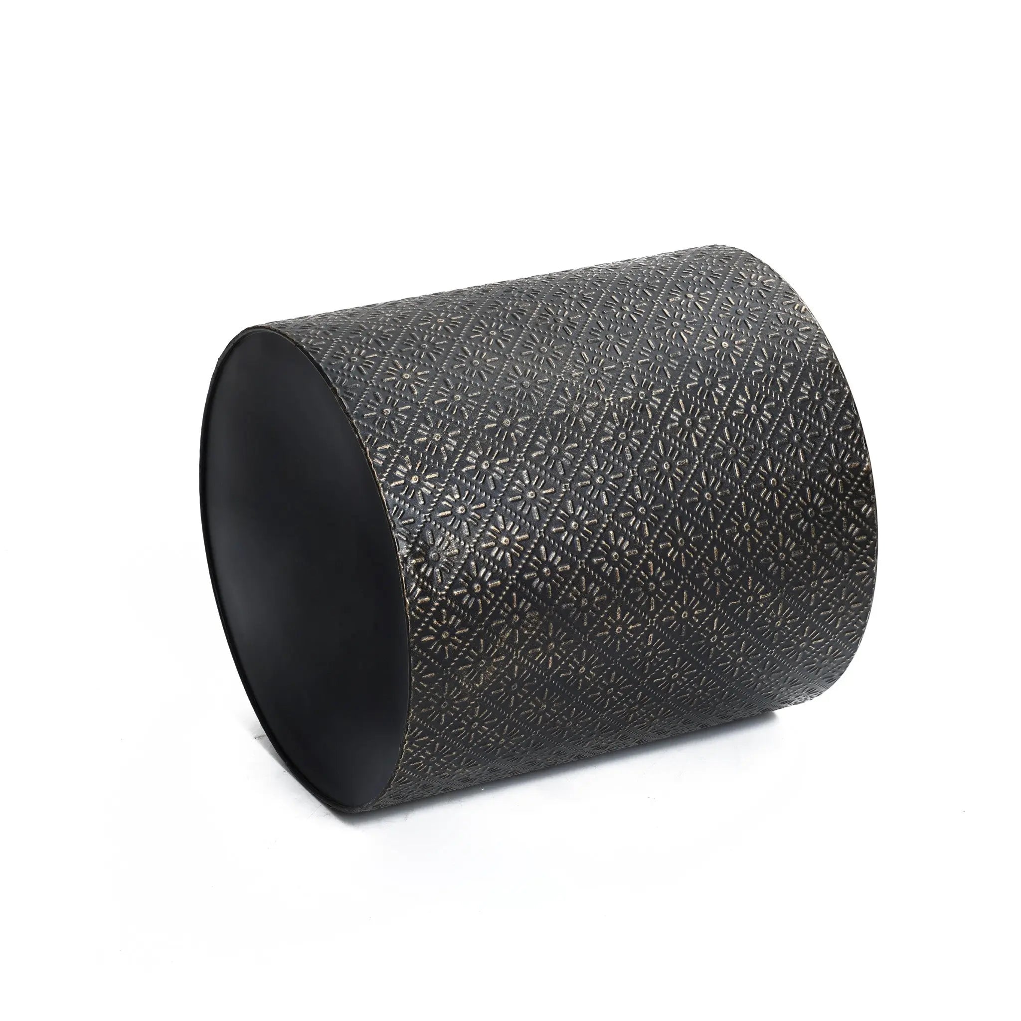 A black cylinder with intricate floral patterns rests elegantly on its side against a plain white background, complemented by a gold metal stand.