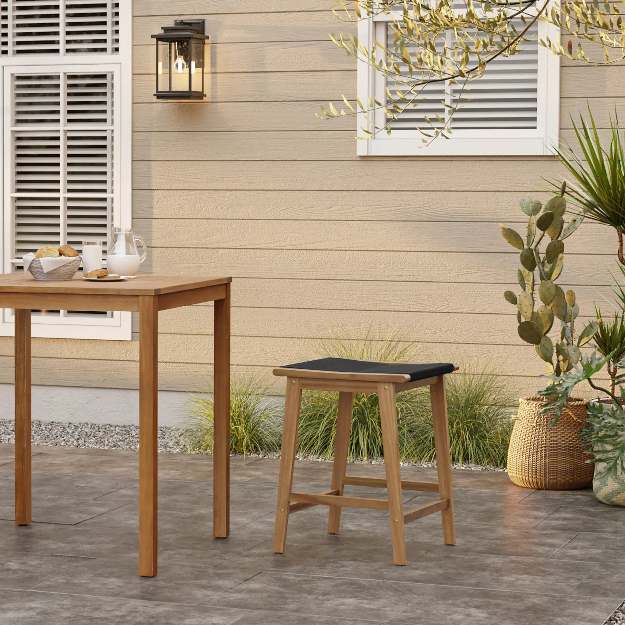 The outdoor patio features a wooden table set for two, complemented by chic black rope-woven seats and a stylish stool. Cactus and potted plants add charm to the scene, while a wall lantern illuminates the beige siding.