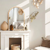 Stylish room with a 34-inch Arch Mirror on a mantel, decorative vases, and a pillow on a chair. Sunlight casts shadows across its scalloped edge framing, with a glimpse of the bed in the reflection.