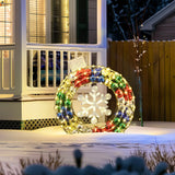 A large, colorful Christmas wreath with a snowflake design is displayed on a porch, its radiant outdoor lights reflecting off the fresh snow. This stunning holiday decoration brings festive cheer to the winter scene.