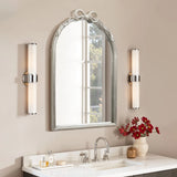 Bathroom vanity featuring an arched silhouette mirror, two wall sconces, a sink, soap dispenser, and red flowers in a vase on a white countertop creates a modern romantic style.