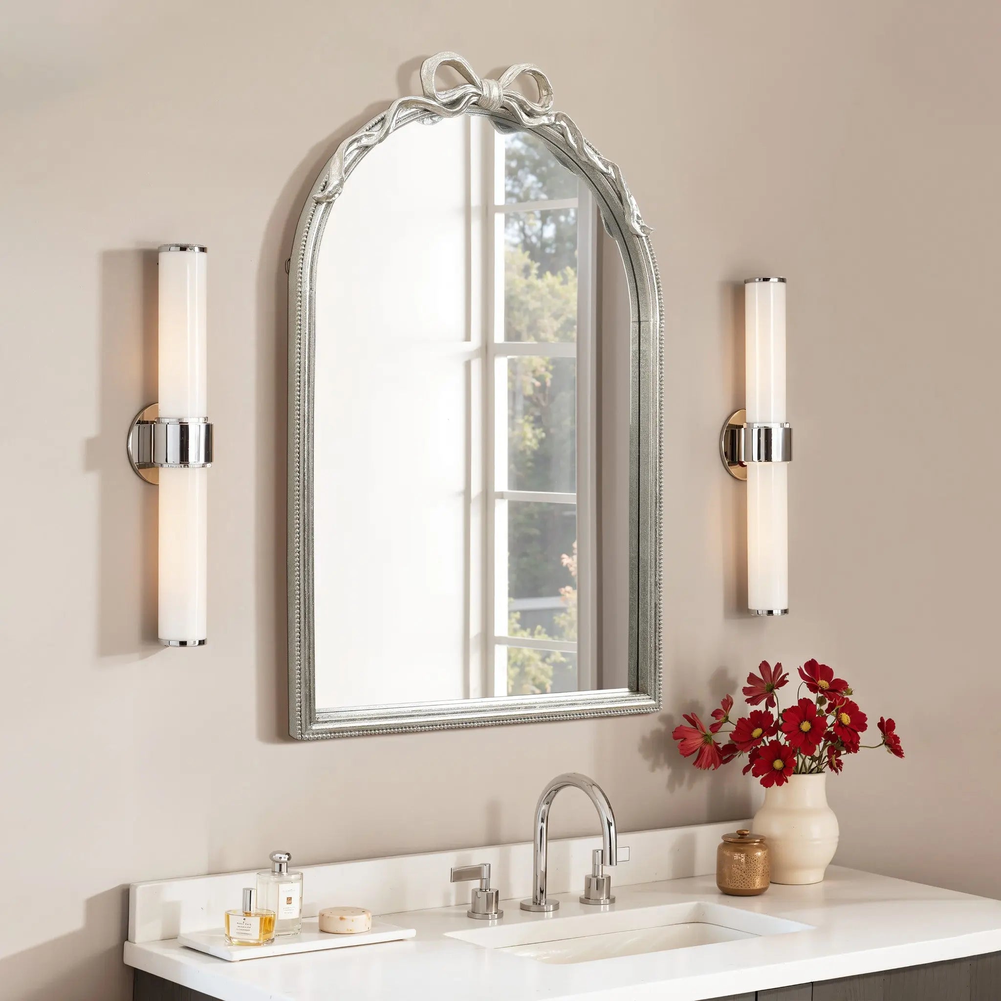 Bathroom vanity featuring an arched silhouette mirror, two wall sconces, a sink, soap dispenser, and red flowers in a vase on a white countertop creates a modern romantic style.