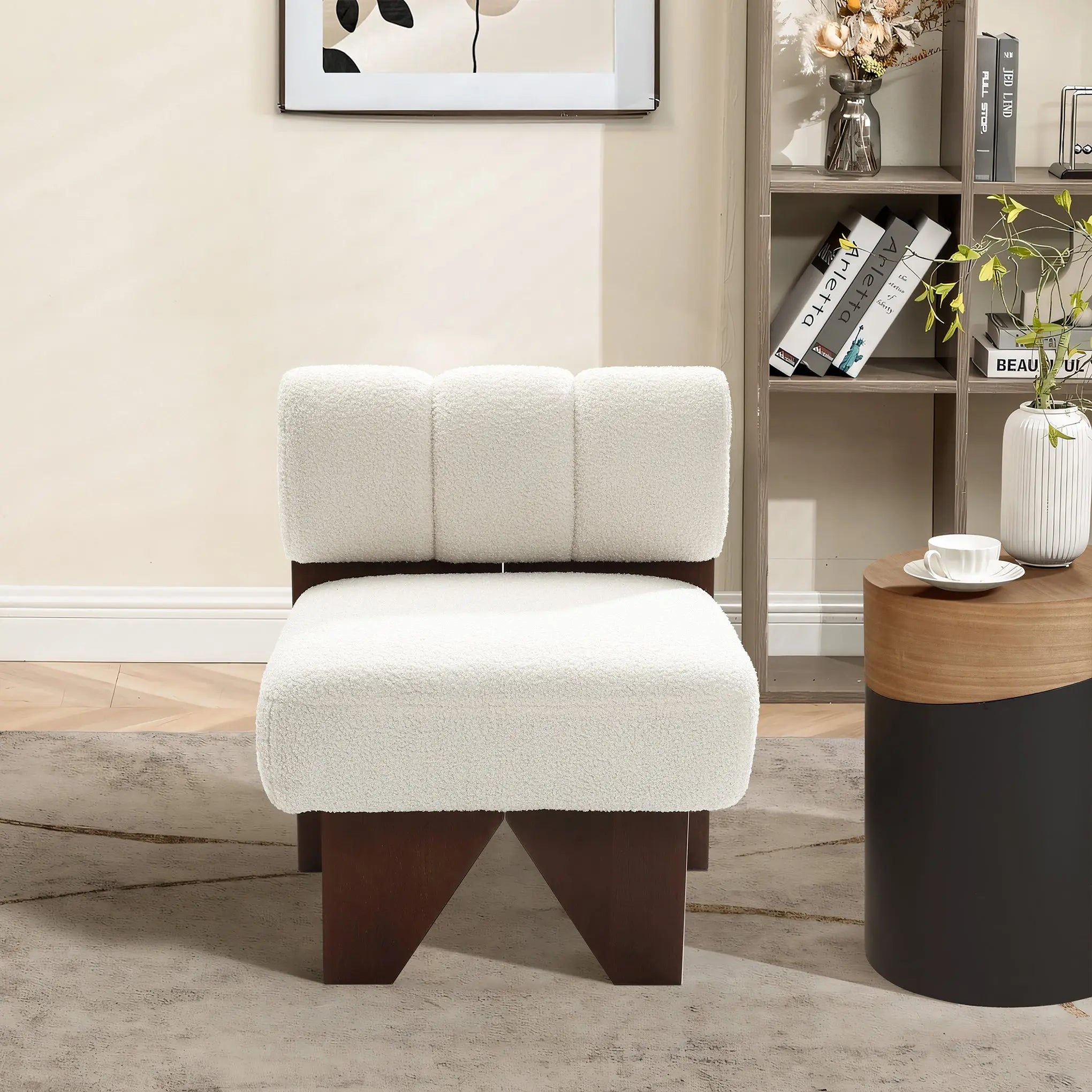 The Lorenzo boucle upholstered wood frame armless accent chair by LuxenHome, featuring a fluffy white cushion and dark wooden legs, adds mid-century allure to the cozy room. Nearby sits a round table with decor, a bookshelf of books and items, and a picture frame on the light-colored wall.
