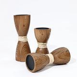 Three handcrafted, wooden hourglass-shaped cups with intricate rattan design and rope details are displayed, two standing upright and one lying on its side.