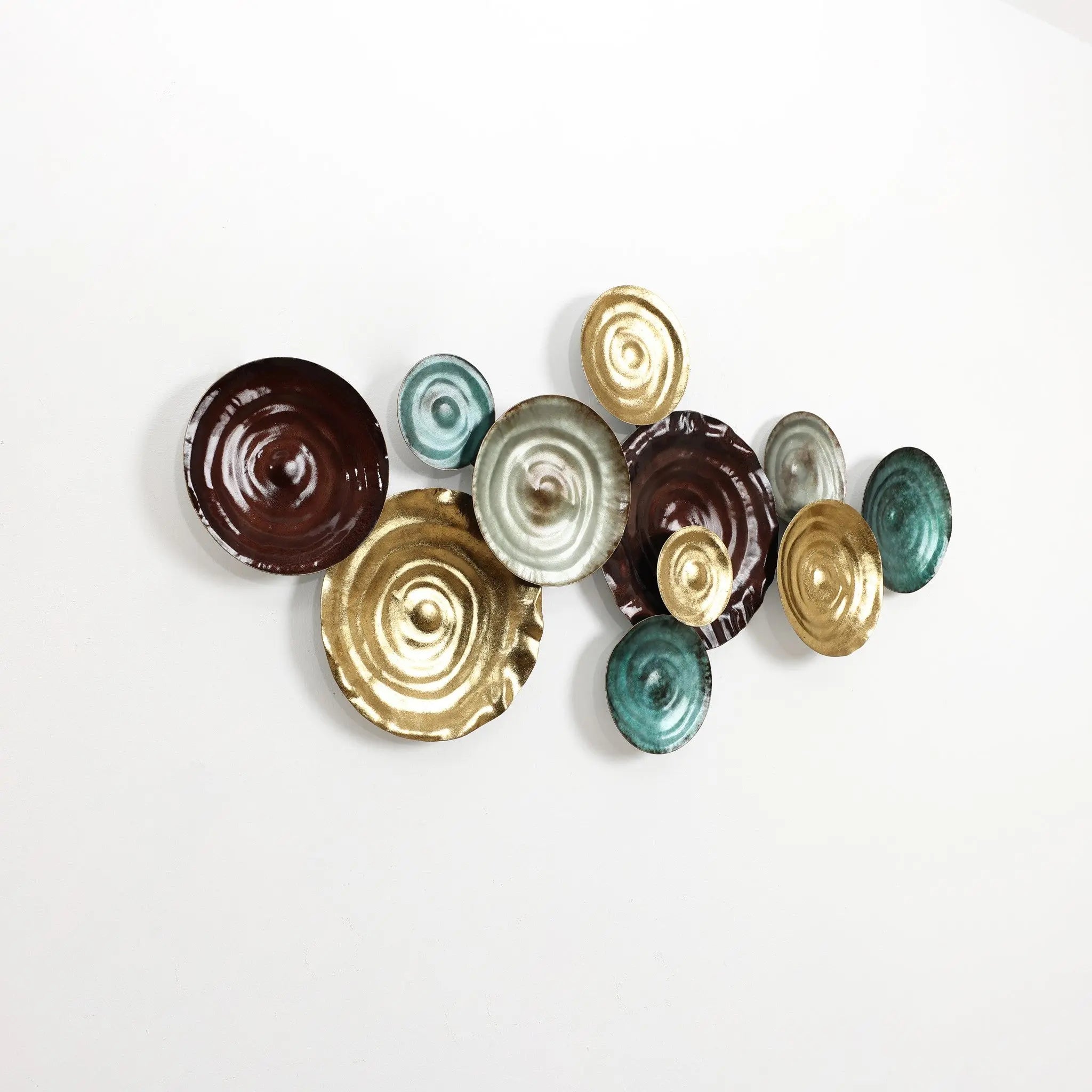 Wall art featuring an abstract design of textured, circular ceramic pieces in brown, gold, and teal hues, mounted against a white background.