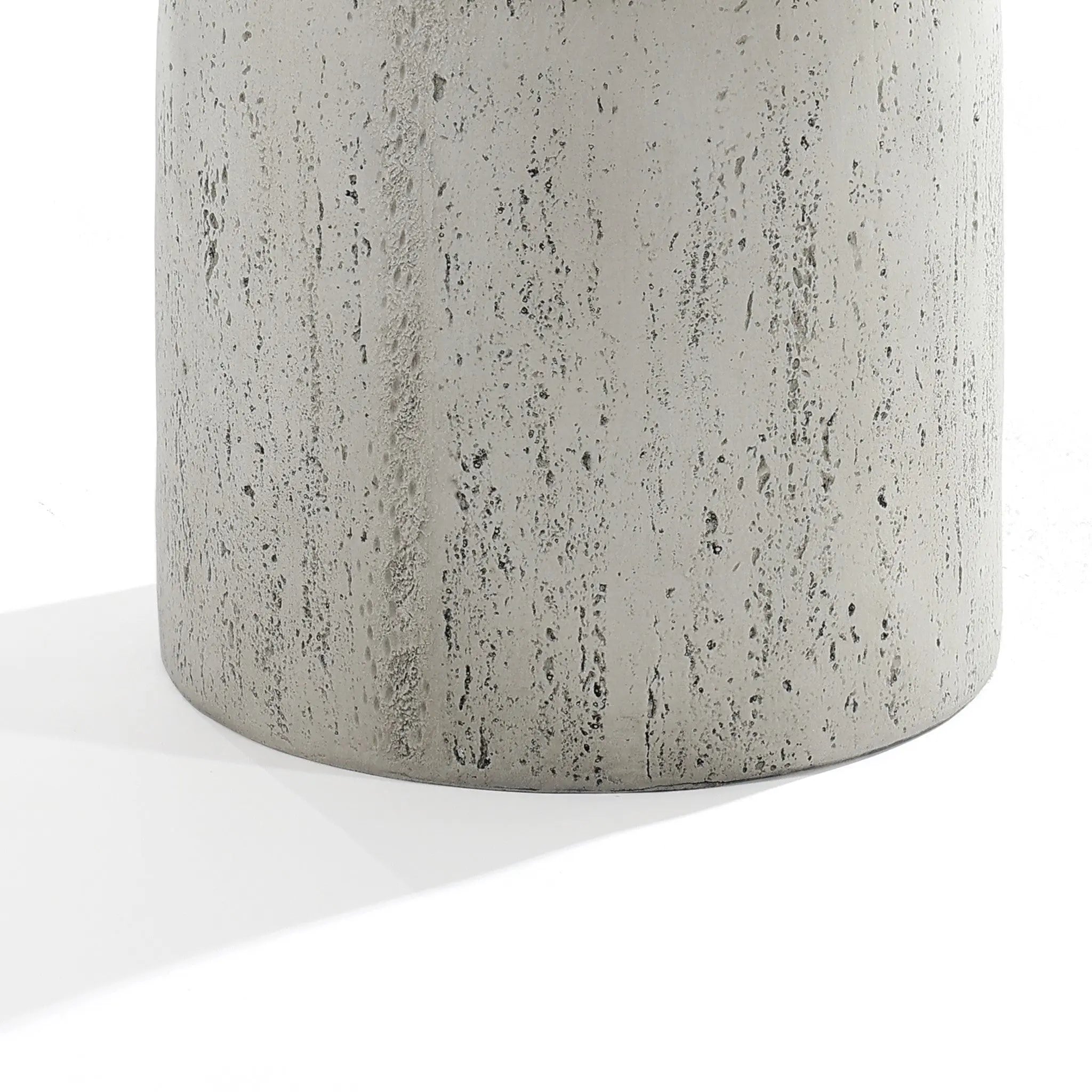 Close-up of the Rustic off White and Gray Outdoor Side Table by LuxenHome, 19.7 h. Crafted from concrete, its textured surface features small pits and grooves, casting a soft shadow against a white backdrop.