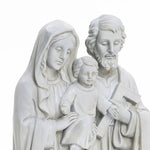 A white, marble-like polyresin sculpture portrays three figures: a seated child in the center, flanked by a woman holding the child and a man with a carpenters square, embodying the essence of religious decor as a Holy Family statue.