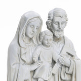 A white, marble-like polyresin sculpture portrays three figures: a seated child in the center, flanked by a woman holding the child and a man with a carpenters square, embodying the essence of religious decor as a Holy Family statue.