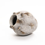 A weathered, round, gray ceramic pot with an uneven surface and scattered brown patches rests on its side against a white background. This handcrafted vintage vase, featuring multiple protruding nubs, adds a touch of versatile home decor to any setting.