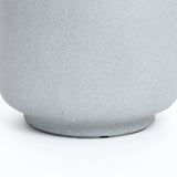 The image displays the lower part of a textured, light gray cylindrical object, possibly a weather-resistant planter or pot with a slightly wider base, resting on a smooth white surface.