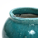 Close-up of a teal ceramic vase with a shiny, textured glaze and a slightly uneven rim, embodying a rustic design. Perfect as an indoor and outdoor jar vase, its organic charm adds character.