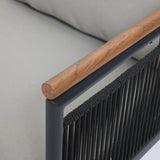 Close-up of a chair armrest featuring a wooden top, black metal frame, and woven black cord sides designed with subtle rope vertical stripes. In the background, a light gray cushion complements the outdoor seating set beautifully.