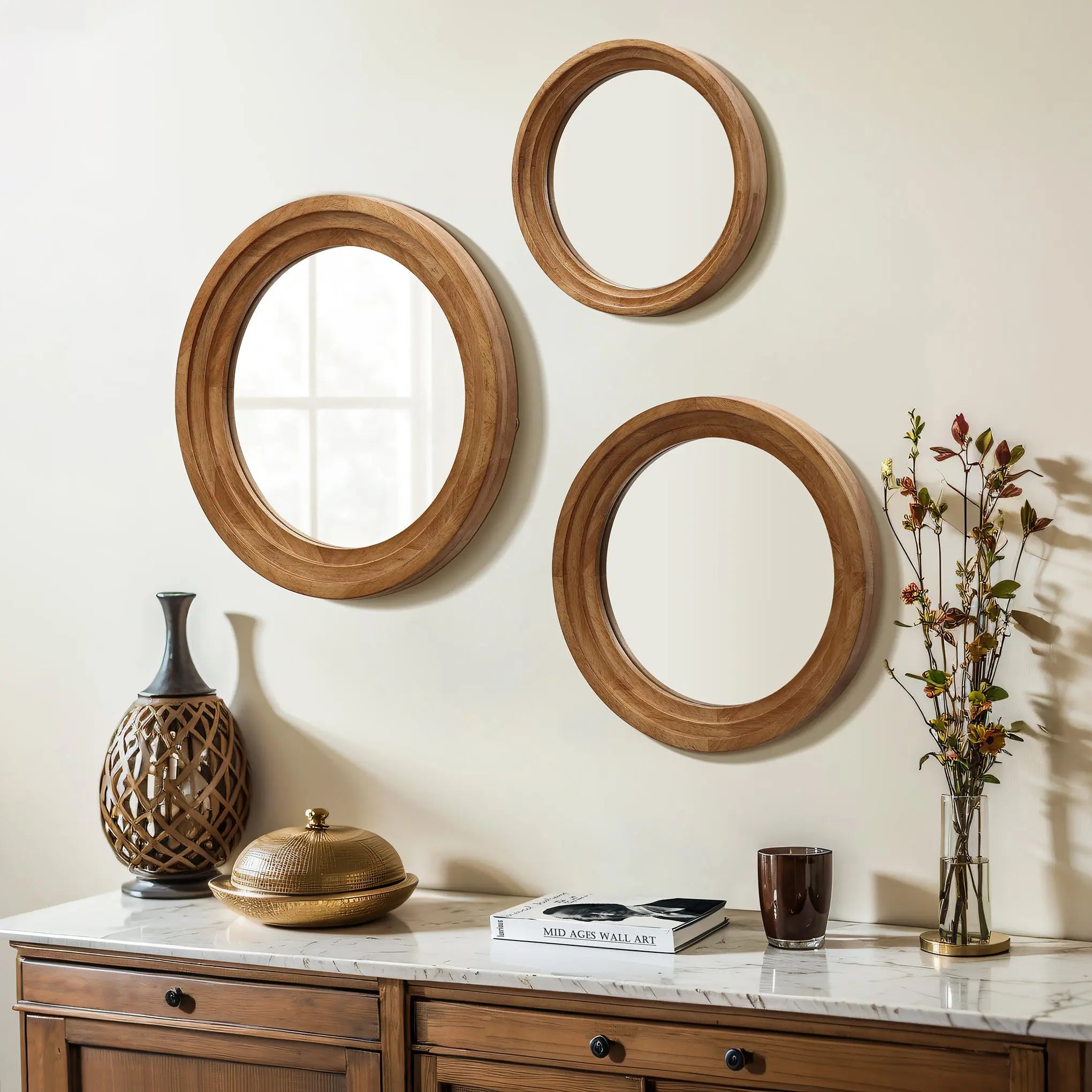A trio of round rubberwood-framed mirrors hangs on the wall above a wooden cabinet. The cabinet displays decorative items such as a vase, a book, a cup, and a branch with leaves and berries, creating an optical illusion of expanded space.