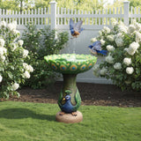 The exquisite Peacock Resin Birdbath graces the garden, surrounded by white flowers. Two birds dance above, one joyfully splashing in the basin, adding charm to the outdoor space.