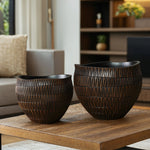 Two dark brown, textured ceramic vases with geometric patterns sit on a wooden coffee table in a cozy living room. A beige couch and a shelf with decorative items, including a stylish small LuxenHome dark brown textured resin round planter, are visible in the background.