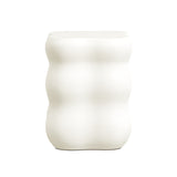 A white, ribbed vase with a wavy, cylindrical shape stands elegantly against a plain background, seamlessly fitting into the realm of modern home furnishings.