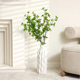 A versatile piece, this elegant ceramic vase with green leafy branches stands on a light-colored floor next to a beige sofa in a sunlit room.