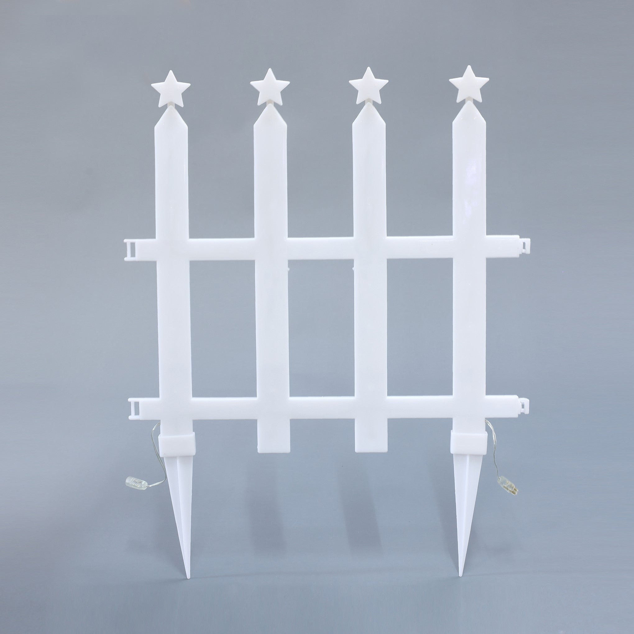 White plastic fence with 4 vertical posts, each topped with star,2 ground stakes the bottom, small electrical wires attached.