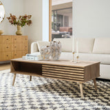 Modern living room with a light wood coffee table featuring dual-side storage, flanked by two vases and candlesticks. A beige sofa and patterned rug complement the decor, while a large window provides natural light.