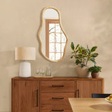 A decorative statement piece, the wooden sideboard crafted from natural pine wood features an irregular oval-shaped mirror, complemented by a lamp and plants. The windows reflection reveals trees outside, enhancing its organic charm.