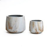 Two ceramic plant pots on a white background; the left one is larger with a round shape, and the right one is smaller, sharing a similar design. Both feature a wood-like textured pattern, reminiscent of an elegant Marble Planter Set suitable for indoor and outdoor spaces.