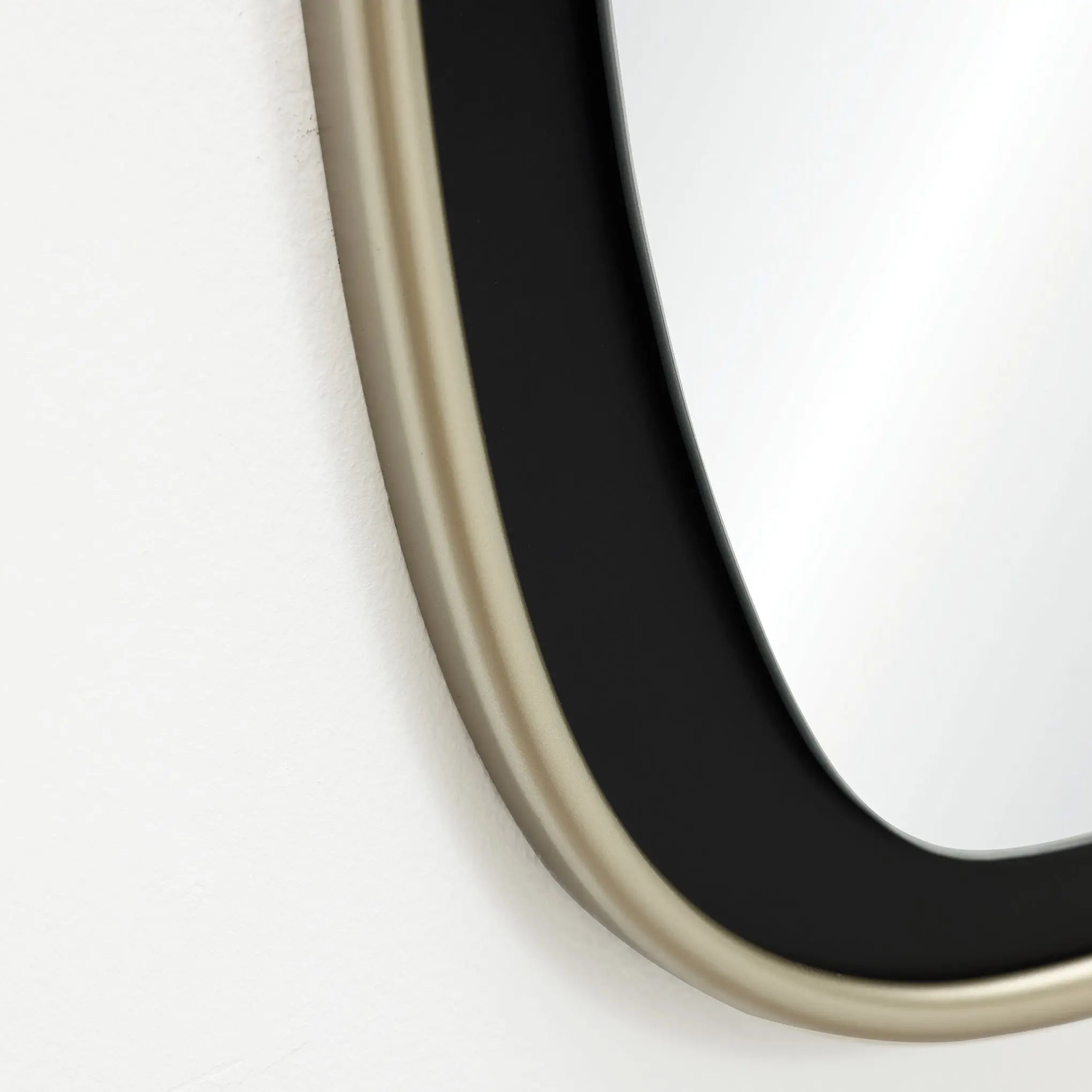 Close-up of a contemporary mirror with an oblong black and gold frame hanging on a white wall.