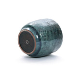 A LuxenHome Marina ceramic planter is on its side, showing its circular base. The dark green planter has a grid pattern with an earthy brown round-bottom base featuring a small central hole.