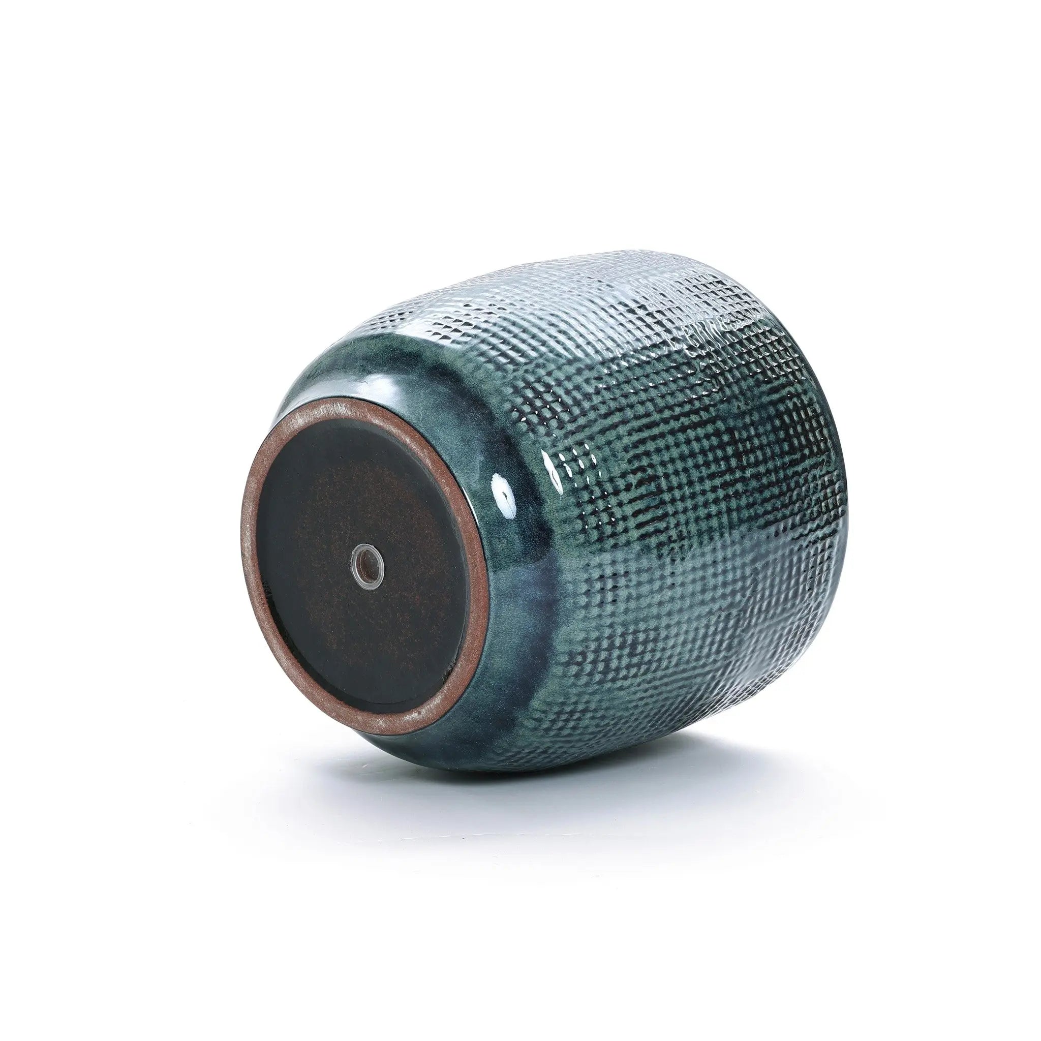 A LuxenHome Marina ceramic planter is on its side, showing its circular base. The dark green planter has a grid pattern with an earthy brown round-bottom base featuring a small central hole.