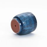 The LuxenHome Ocean blue glazed round ceramic planter, 11.22 h, featuring a deep blue checkered pattern and brown base, is showcased on its side against a white background with striking gradient color transitions.