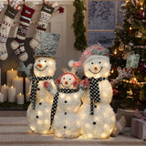Three lighted snowmen with black and white scarves stand in front of a Christmas tree and fireplace decorated with stockings and candles, creating a charming snowman decoration perfect for your outdoor Christmas decor.