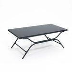 A black rectangular folding table with a metal frame and flat top is elegantly paired with an outdoor seating set, creating a sleek contrast against the plain white background.